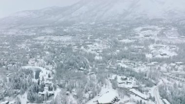 Noel ve Yeni Yıl arkaplanı 4K USA. Colorado 'nun küçük beyaz bir kasabasında taze karla kaplı düz caddelerin ve çatıların yukarıdan görünüşü. Soğuk kış gününde Aspen karlı köyünün insansız hava aracı antenleri