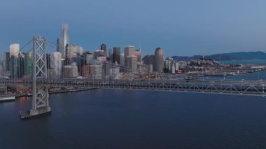 San Francisco şehir merkezindeki Financial District gökdelen ofis binalarında, Bay Bridge 'in manzara manzarası. Sabah gündoğumunun 4K b-roll drone görüntüsü. Aydınlatılmış şehir ABD