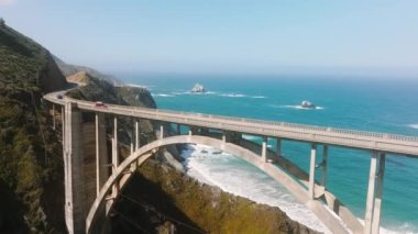 Cinematic airy bridge with arch architecture and scenic seascape view on beautiful amazing light blue Pacific ocean. Tourists driving in cars by scenic route on summer vacation road trip by California