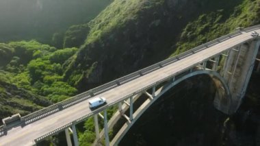 Aerial view tourists cars travel in beautiful mountainous terrain with breathtaking rocky ocean coast views. Cars driving on highway road with beautiful nature landscape in golden sunshine light USA