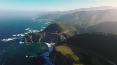 Scenic arch bridge at the pure nature of Big Sur park. Panoramic aerial view over the rocky ocean coast at sunset. Beautiful ocean water meets the rocky shore. 4K mountains on motion background, USA
