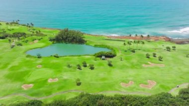 Aerial view of Golf course on Kauai coastline, Hawaii island. Establishing shot, drone flying over golf club. Summer morning footage, summertime, sunlight view. Scenic pacific ocean shore green field
