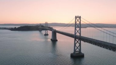 Flying above San Francisco Bay with monumental architecture of Bay Bridge road with easy traffic on summer sunny sunrise. Amazing pink sunrise sky, Aerial background with copy space, California USA