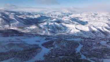 Aerial forward Epic winter snow-covered mountains surrounding Snowmass village ski resort, Colorado abstract natural landscape. Ski slopes on mountain terrain. Cinematic sunny winter day background