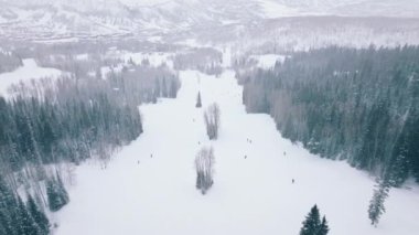 Cold winter day high up in mountains, Snowmass ski resort. Ski show great winter panorama 4K. Ski aerial of fast skiers in beautiful mountain forest landscape riding down snowy slope with high speed