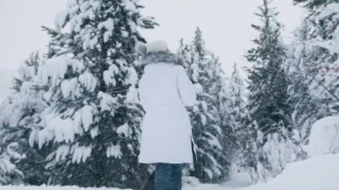 Camera follows woman on trip or adventure. Young millennial traveller walking in beautiful mountain forest on winter vacation and creating holidays memories. Concept Christmas travels in slow motion