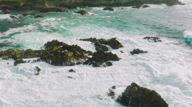 Colorful water of Pacific ocean, swirl above rocky and scenic coastline. Sea waves breaking over rocks. Spectacular sea storm in Monterey coastline, California, USA. Sea waves crashing on coastal rock