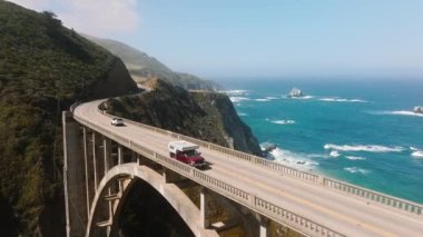 People traveling in camper van by scenic ocean route by American West Coast. Tourists exploring California shore in Big Sur park with cinematic landscapes and beautiful nature. Aerial bridge traffic