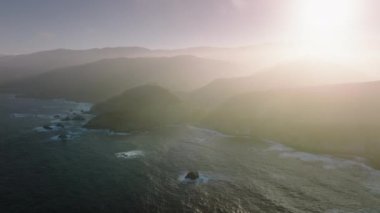 Cinematic aerial shot of scenic mountains covered by sunny glowing cloud of ocean breeze. Summer vacation dream travel, road trip by cinematic nature landscape at Big Sur on West Coast, California USA