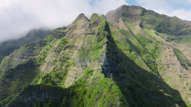 Drone shot flying over beautiful mountain ridge and clouds in rural jungle bush forest of Kokee park on Napali coast on Kauai island of Hawaii viewing jungle and scenic peaks with clouds on background