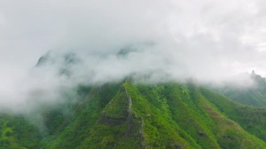 Aerial shot flying in the clouds covering green mountain peaks on Na Pali coast National park, in Kauai island, Hawaii state, USA. Cinematic scenery tropical rainforest climate during global warming