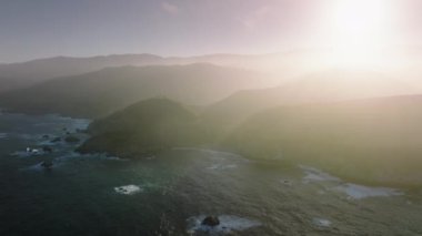 Highway 1 through the coastline by the Pacific Ocean. Aerial view of California Scenic Byway with sunset skyline in the background. High quality 4k footage