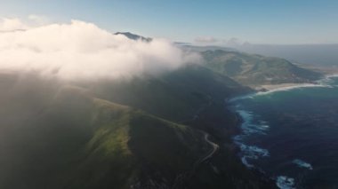 Pristine land where the ocean meets the lush green landscape with steep cliffs. Aerial view of Bixby Creek with inland, scenic route. High quality 4k footage