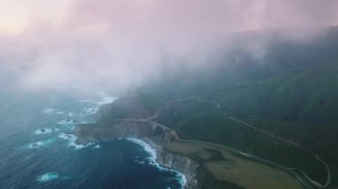Cloudy purple skyline above cinematic ocean and greenish forests. Aerial view of cinematic landscape, washed with Pacific Ocean in Big Sur, California, USA. High quality 4k footage