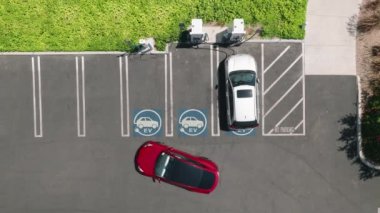 Aerial view of red car parking in green business park. 4K electric, zero pollution cars on green energy concept on modern city parking lot. Alternative energy for ecological cars at bright sunny day