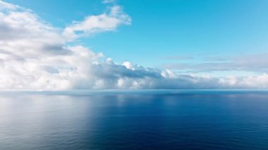 Epic flight over perfect deep blue sea with scenic white clouds in blue sky. Endless horizon seen in distance, cinematic blue depths of perfect calm ocean. Beautiful calm sea, evening sky background
