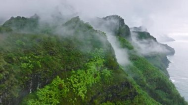 Flying through rain clouds above green mountain tops covered by tropical jungle rainforest. High peaks at Na Pali coast park, wonderful rainy summer day natural landscape.Epic Hawaii island background