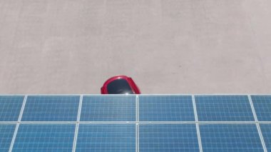 4K electric, zero pollution car on green energy concept on modern city parking lot. Alternative energy for ecological cars under blue solar batteries. Aerial view red car parking under solar panels