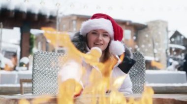 Woman in red Christmas hat roasting marshmallows in fire pit having after ski fun leisure activity at Winter holiday ski resort in Apsen. POV video of young woman grilling marshmallow stick in bonfire