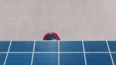 4K electric, zero pollution car on green energy concept on modern city parking lot. Alternative energy for ecological cars under blue solar batteries. Aerial view red car parking under solar panels