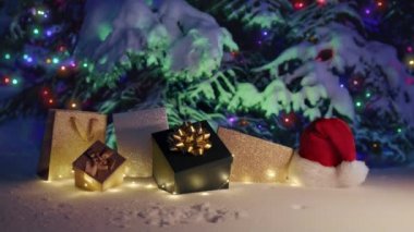 Happy New Year 2023 golden glitter gift boxes and present bags on colorful light garland on snowy tree blurry background. Merry Christmas eve concept winter miracle night footage. RED camera 6K shot