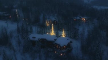 Christmas and New Year Background. Night Magic Snowy Forest on blue night. Christmas Night in the mountain village with bright illuminated Christmas trees. Beautiful aerial above mountain chalet 4K