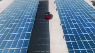 Aerial red electric car on rooftop parking with solar panels. Zero pollution car, green energy concept on modern rooftop parking lot. Alternative energy for ecological cars under blue solar batteries