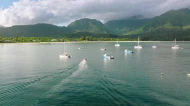 Aerial drone video tropical paradise exotic island bay with cinematic tropical jungle mountains landscape and emerald crystal clear ocean with moored yachts and sail boats in Hawaiian destination 4K