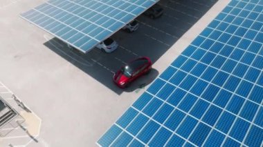 Aerial red electric car on rooftop parking with solar panels. Zero pollution car, green energy concept on modern rooftop parking lot. Alternative energy for ecological cars under blue solar batteries