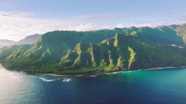 Drone footage of the cliffs with ancient green trees and flowers. Crystal clear, calm waters washing Haena Beach with towering majestic mountains. High quality 4k footage