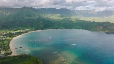 Aerial footage of a beautiful beach, surrounded by mountains. A panoramic shot of the Hanalei Bay with lavish rainforest and steep mountains. High quality 4k footage