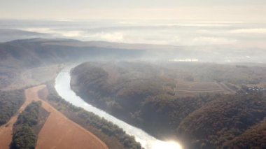 Gorgeous autumn season at beautiful landscape with vibrant green trees. Fresh morning fog above the river shores and mountainous backcountry in the background. High quality 4k footage