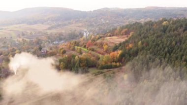 Drone footage of the hilly landscape above a town below foggy skyline. Spectacular, romantic scenery of remote village surrounded with deep colorful forest. High quality 4k footage