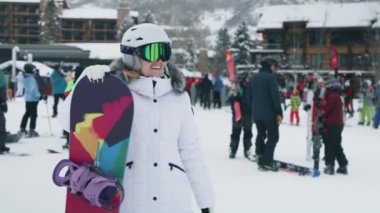 Girl having fun in Aspen waving hand to friends in slow motion. Happy young woman downhill the ski slope making a picture or video with snowboard at ski resort in snowy mountains enjoying vacation 6K