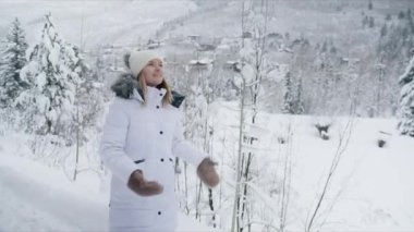 Woman walking by forest trail in winter wonderland mountain village on blurred background. Portrait of attractive happy blonde woman smiling cheerfully. People outdoors enjoying Aspen at winter 6K