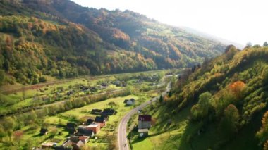 Colorful leaves covering steep hillside with a village in the background. Drone footage of cinematic backcountry with winding highway and charming cottages. High quality 4k footage