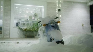 Stylish old fashioned moto scooter under white snow. Winter wonderland background in slow motion shot on RED camera. Christmas holidays vacation footage with small town village covered with fresh snow