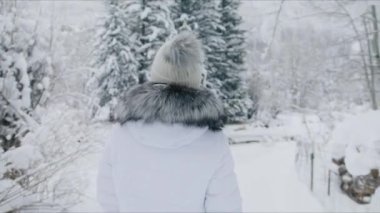 Close up back view woman on winter trip or adventure. Traveller walking in beautiful mountain forest on winter vacation and creating magic holidays memories. Christmas travels concept in slow motion