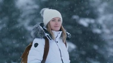 Portrait of nice looking caucasian European beautiful female person. Young woman in casual outwear looking around with green spruce forest covered by fresh snow on blurred background. Female portrait