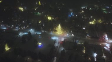 Aerial of snow falling on Christmas tree illuminated for holidays. Snowflakes falling on city streets. Christmas American city illuminated with holiday lights. Aspen ski resort village on winter night