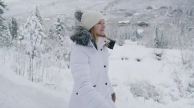 Portrait of attractive happy blonde caucasian woman smiling cheerfully, walking by forest trail in winter wonderland mountain village on blurred background. People outdoors enjoying Aspen at winter 6K