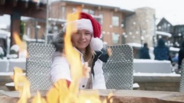 Kışın şenlik ateşinde kızaran çubukta lokumlu beyaz bir kadın eli. Aspen 'deki modern lüks kayak köyünün şöminesi. Kırmızı Noel Baba şapkalı kadın Amerika 'da tatil yapıyor.