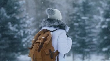 Active healthy woman with tourist backpack taking into woods. Female traveler on green fir forest blurry background, 6K RED camera. Slow motion woman hiking in forest on snowy winter day
