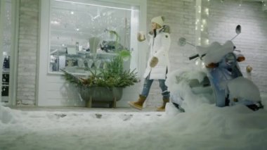 Winter holiday vacation, 6K Video. Woman drinks tea cup while walking by terrace at town village on winter snowy night. Christmas atmosphere, magic feeling, holiday decorations, miracle expectation