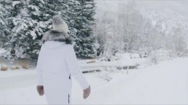 Traveller in fur mittens walking in beautiful mountain forest on winter vacation and creating magic holidays memories. Christmas travels slow motion. Side view woman on winter trip or adventure
