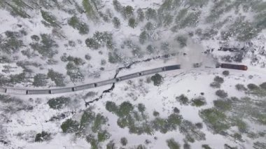 4K Aerial overhead view steam locomotive goes over winter snowy woodland. Follow shot, moving left. Snowy winter day Colorado canyon. Top down aerial shot of railway train in snow covered forest trees