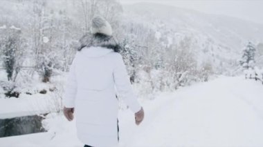 Kamera, sıcak kürk eldivenli kadını kış nehri boyunca yürürken izliyor. Genç gezgin kış tatilinde güzel dağ ormanlarında yürüyor ve tatil anıları yaratıyor. Noel gezileri konsepti