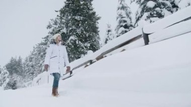Neşeli kız kış gününün tadını çıkarıyor. Dışarıda neşeli duygular besleyen tasasız bir kadın. Yavaş çekim kış konsepti. Güzel sarışın kadın tatilde karlı kırlarda yürüyor.