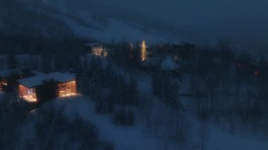 Mavi gecedeki Gece Sihirli Karlı Orman. Dağ köyünde aydınlık Noel ağaçları olan bir Noel Gecesi. Dağ evi 4K 'nin üstündeki hava çok güzel. Noel ve Yeni Yıl Arkaplanı