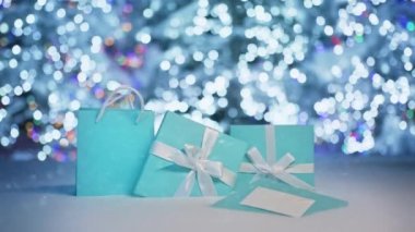 Yeni yılın kutlu olsun. Beyaz kurdeleli zarif mavi hediye kutularının üzerinde kar yağışı var. Karlı bir gece, parlak mavi ışıklar Noel ağaçlarında parlıyor bulanık arka planda parıldıyor
